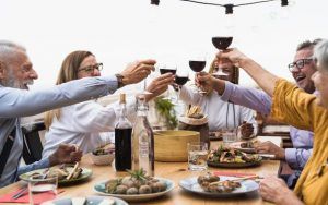 Multiracial senior friends having fun dining together and toasting with red wine on house patio dinner - Food and holidays concept