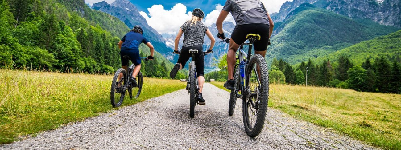 Three people cycling on a dirt track leading into the mountains.