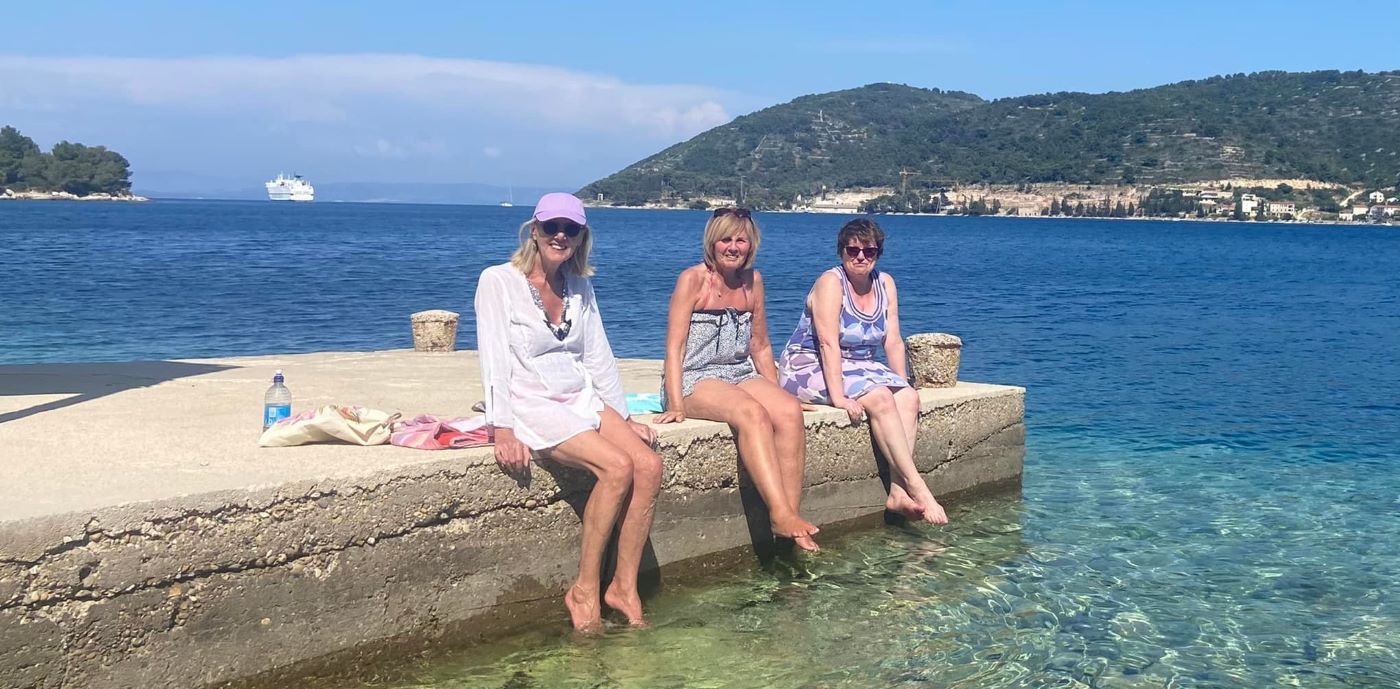 Three woman smiling sitting dipping their feet into the ocean in Croatia